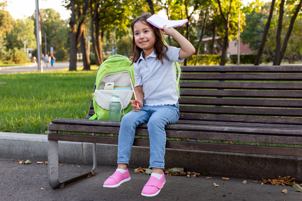小女孩背着书包，坐在公园长椅上打开笔记本。图片下载