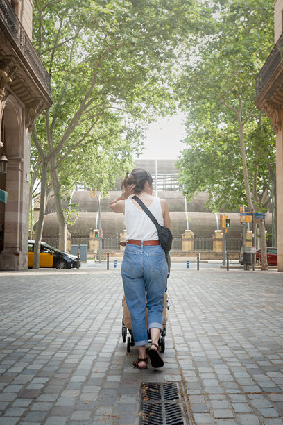母亲推着婴儿车走向城市公园的竖拍照片图片下载