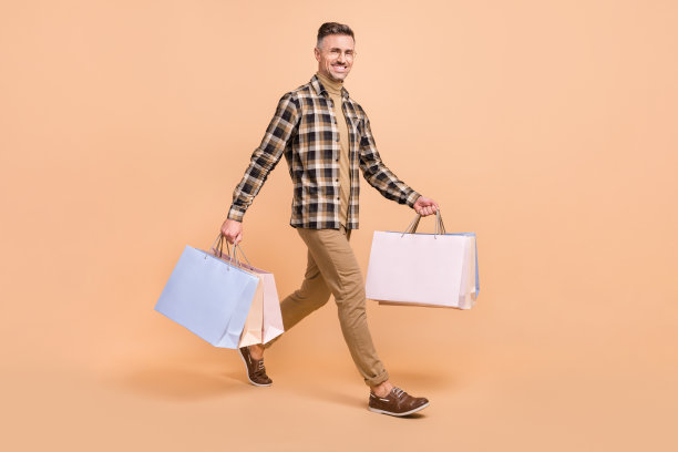 成熟男性全身侧面照片，手持包裹，进行送货服务，背景为米色。图片下载