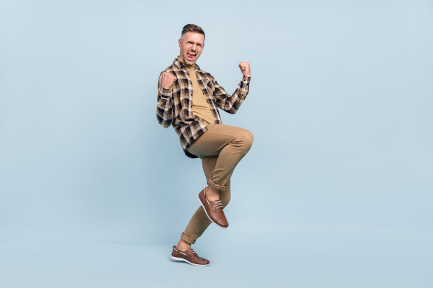 成熟男性全身侧面照片，因中彩票而欢欣鼓舞，双拳紧握，背景为灰色。图片下载