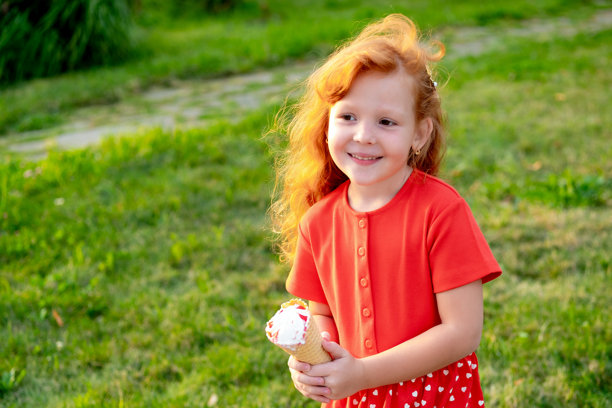 一个小女孩在公园的绿草坪上吃冰淇淋，明亮的夏季儿童假日照片，小女孩在夏天欢笑玩耍。图片下载