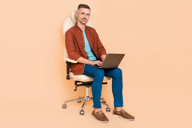 全身照片，市场营销人员坐在皮椅上，使用笔记本电脑输入创业报告，背景为柔和的米色。图片下载