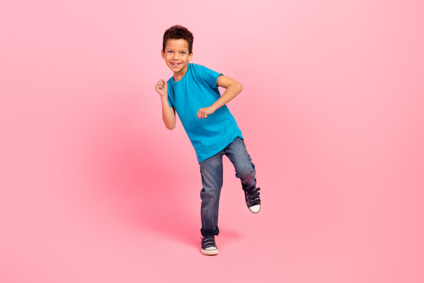 可爱无忧的小男孩穿着蓝色T恤在粉色背景下尽情跳舞，享受乐趣的全身照片图片下载