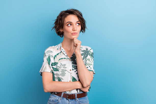 漂亮年轻女孩的照片肖像，手托下巴，思考着，目光空洞，穿着时尚的印花叶子服装，背景为蓝色。图片下载
