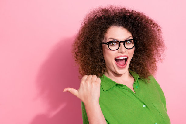 可爱的年轻女士的照片肖像，兴奋地指向空旷的地方，张嘴，穿着时尚的绿色服装，背景为粉色。图片下载