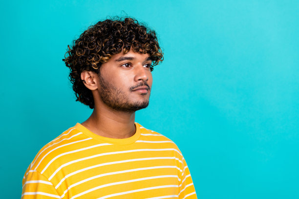 年轻男性的照片肖像，穿着时尚的条纹黄色服装，面带微笑，目光投向空旷的空间，背景为水绿色，适合销售促销。图片下载