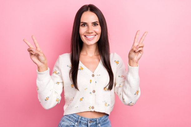 展示双V手势的拉丁裔迷人女孩模特的头像照片，充满乐趣和友好的氛围，背景为粉色。图片下载