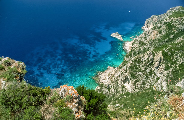 扫描的历史彩色照片，展示了希腊科孚岛帕莱奥卡斯特里察沿海地区的岩石和山脉，阳光明媚。图片下载