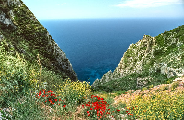 扫描的历史彩色照片，展示了希腊科孚岛帕莱奥卡斯特里察沿海地区的岩石和山脉，阳光明媚。图片下载