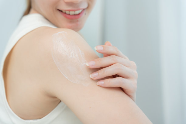 美丽的亚洲女性微笑着涂抹护肤霜。健康的女性为身体涂抹护肤霜。护肤霜广告，抗皱、婴儿般的面容、美白、保湿、收缩毛孔精华。图片下载
