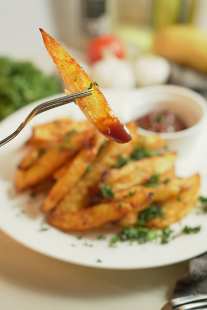 用叉子夹着烤土豆，撒上红椒粉和大蒜，点缀新鲜香菜和浓郁的番茄酱，这是一道令人无法抗拒的自制美食，刚从烤箱中取出。竖版照片图片下载