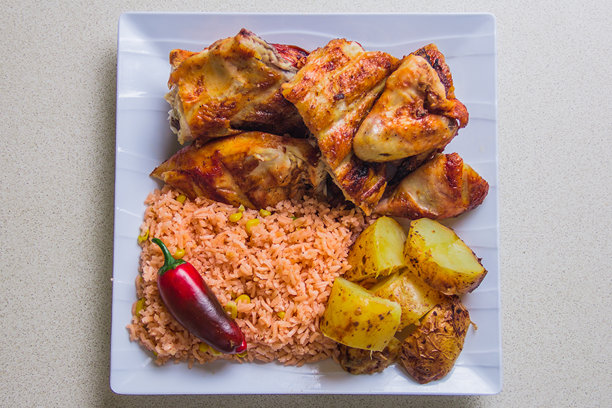 丰盛的餐点，包含烤鸡、香喷喷的米饭和烤土豆，精美地摆放在盘子上，适合展示舒适食品和美食的库存照片。图片下载