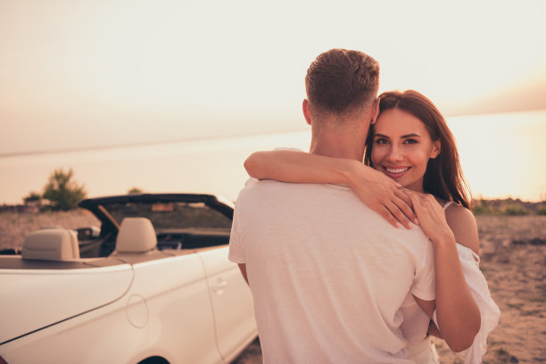 夏日黄昏时分，情侣在海边沙滩上相拥而笑的照片肖像图片下载