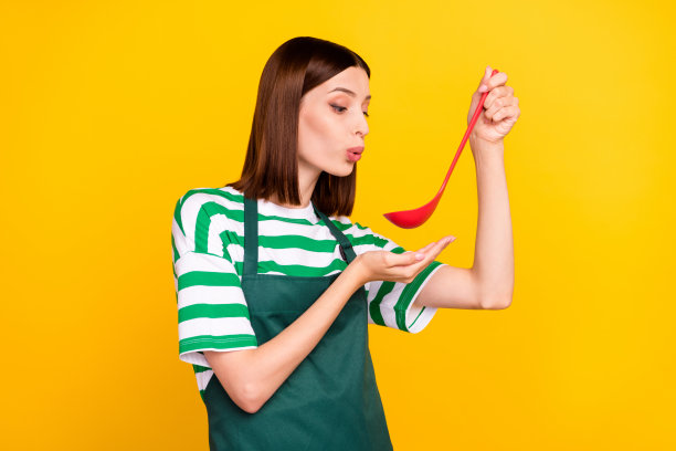 穿着条纹T恤和围裙的年轻棕发女士在黄色背景下做晚餐的个人资料照片图片下载