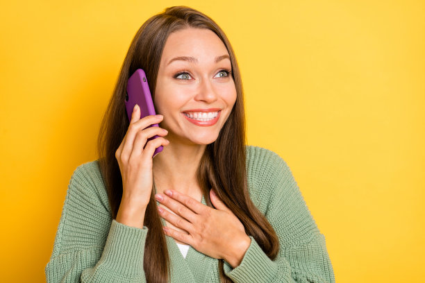 兴奋的女性触摸胸部，手持电话，背景为鲜艳的黄色，留有空白空间的照片肖像图片下载