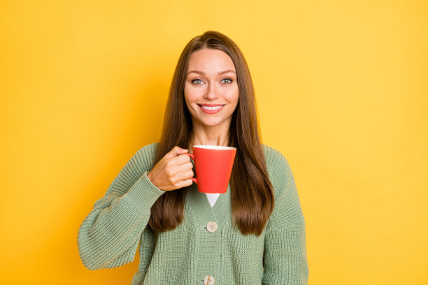 女人手持大红色杯子的照片肖像，背景为鲜艳的黄色。图片下载