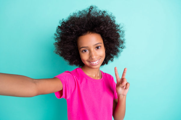 微笑的非裔美国女孩在鲜艳的青色背景下做出V字手势自拍的照片肖像图片下载