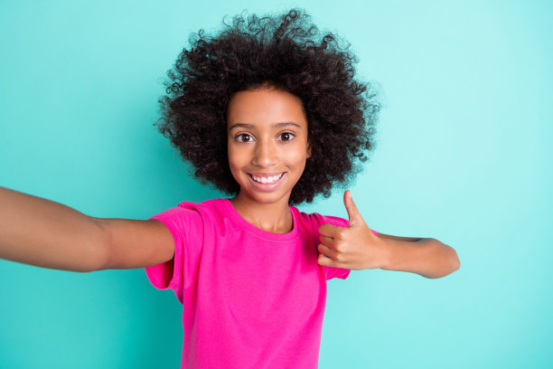积极的非裔美国女孩在鲜艳的青色背景下竖起大拇指自拍的照片肖像图片下载