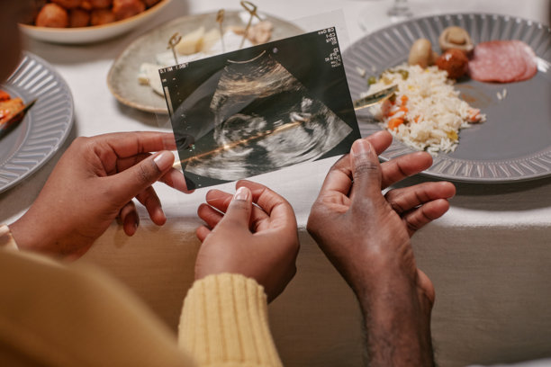 父母在餐桌上期待着宝宝，手里拿着超声波照片图片下载