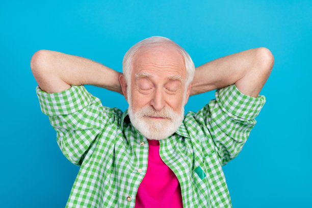 高角度俯视照片，老态龙钟的爷爷双手抱头，放松地坐在蓝色背景下。图片下载