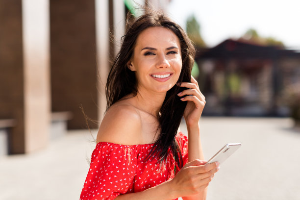 迷人且吸引人的年轻女性在户外街道上走路，手持手机拍侧面照片，作为博主。图片下载