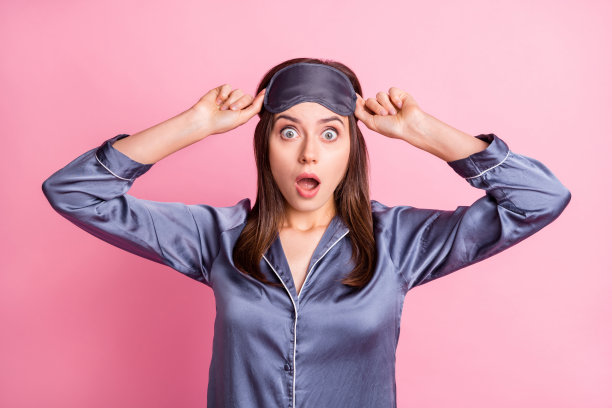 惊讶的女性用双手触摸面具的照片肖像，背景为柔和的粉色。图片下载