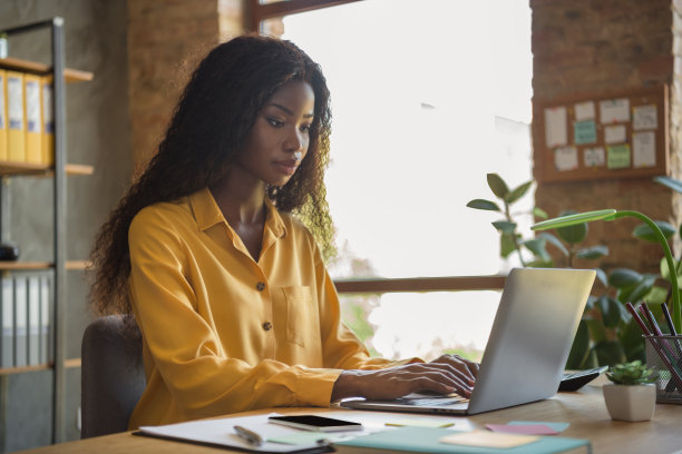 严肃的深肤色棕发女商人在办公室桌子上打字的侧面照片，室内工作环境。图片下载