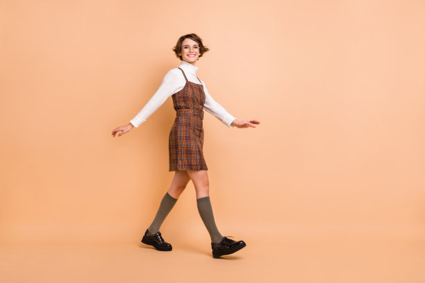 年轻漂亮快乐积极微笑的女学生在柔和色彩背景下走路的全身侧面照片图片下载