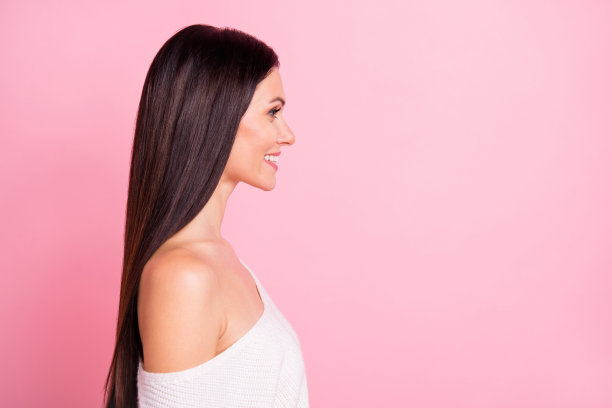 年轻可爱漂亮的微笑女孩侧面照片，长发完美，背景为粉色。图片下载