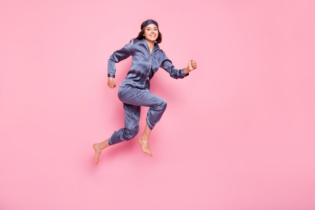 侧面全身肖像照片，戴着眼罩的女性在粉色背景上跳跃奔跑。图片下载