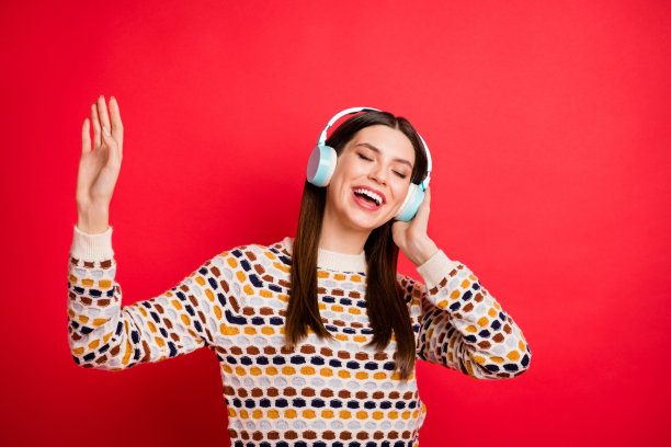 梦幻女孩的照片肖像，戴着蓝色耳机，微笑着唱流行单曲，背景为鲜艳的红色。图片下载