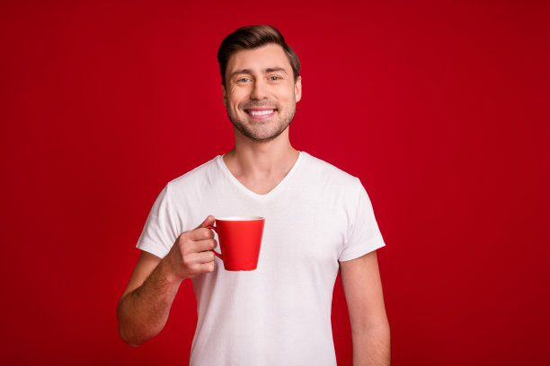 年轻微笑的男士在鲜艳红色背景下，手持咖啡杯休息的照片肖像图片下载