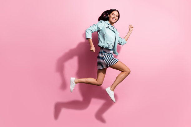 穿着蓝色夹克的可爱年轻女孩在粉色背景下匆忙奔跑跳跃的全身照片图片下载