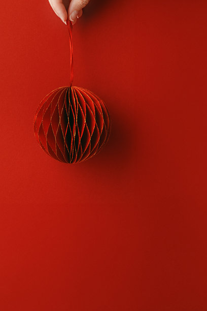 节日红色纸质圣诞装饰品，女性手中悬挂的红色球体，红色背景上的蜂窝状斯堪的纳维亚装饰，简约单色照片，创意节日俯视图图片下载