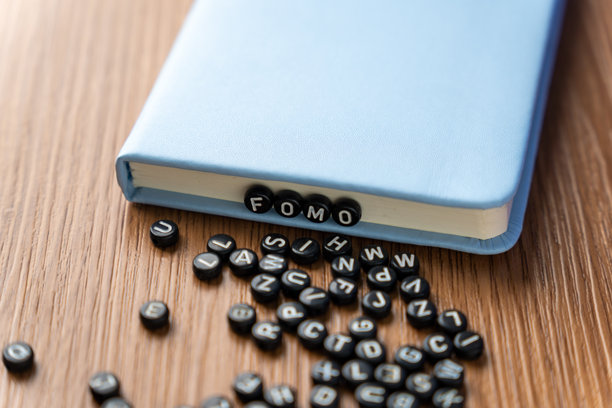 字母珠子拼写FOMO，周围散落着更多珠子，放在木桌上。图片下载