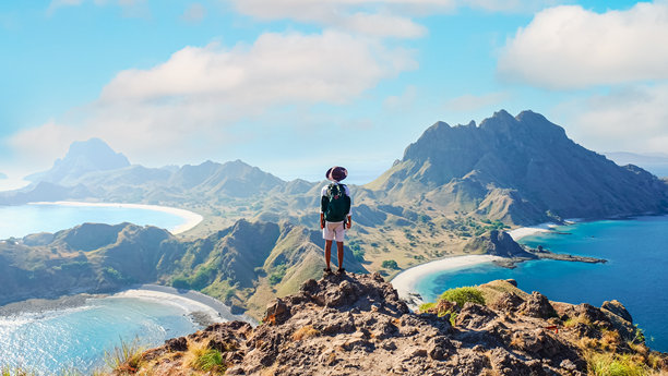 在印度尼西亚科莫多国家公园的帕达尔岛上，冒险者站在山丘上，背景是蓝色海洋和崎岖的山脉。理想的夏季旅行与探索素材。图片下载