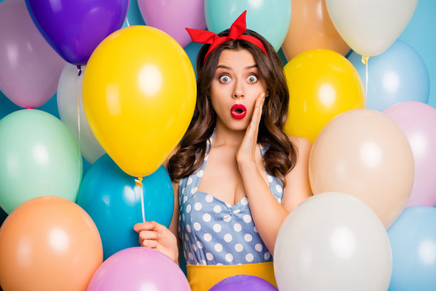 惊讶的疯狂女孩在精彩的派对活动中看起来很棒，令人印象深刻，尖叫着“哇，天哪”，手里拿着明亮的氦气球，头戴发带，身穿裙子，背景是五彩斑斓的气球。图片下载