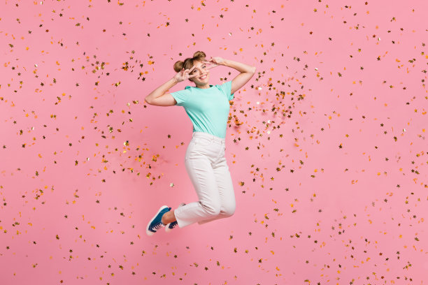 全身照片，轻松自在的人双手比V字手势，靠近眼睛，穿着青绿色，背景为粉色。图片下载