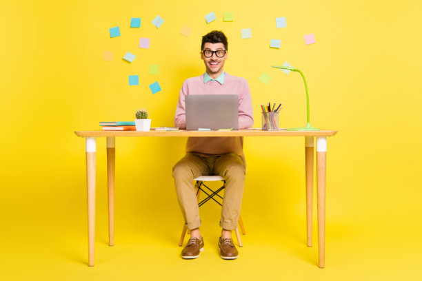 年轻帅气的男人在黄色背景下微笑着使用笔记本电脑远程工作的大尺寸照片图片下载
