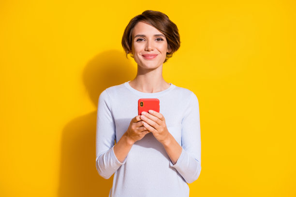 快乐女性双手握着手机的照片肖像，背景为明亮的黄色。图片下载