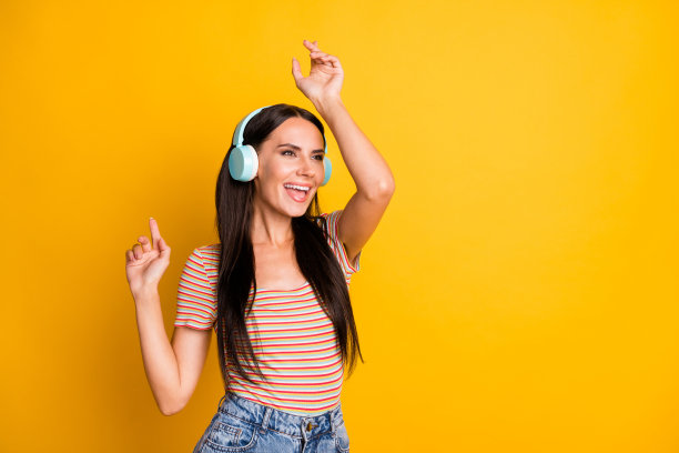 快乐女孩的照片肖像，戴着耳机，听着流行单曲，唱着歌，目光空洞，背景为明亮的黄色。图片下载