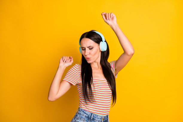 戴着耳机的快乐女孩在明亮的黄色背景下跳舞，听着热门歌曲并唱歌的照片肖像图片下载
