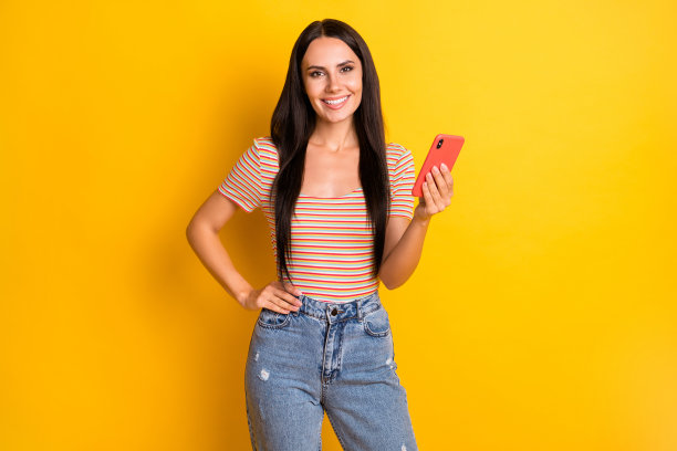 女性网红在鲜艳的黄色背景下微笑着阅读手机信息的照片肖像图片下载