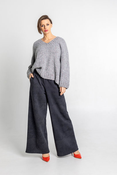 模特外貌的美丽女性肖像。女孩穿着灰色毛衣、黑色裤子和红色鞋子，背景为灰色。时尚妆容的漂亮女性在摄影棚中摆姿势。竖版照片图片下载