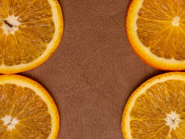 照片展示了一半橙子的表面细节，放置在棕色皮革表面上。图片下载