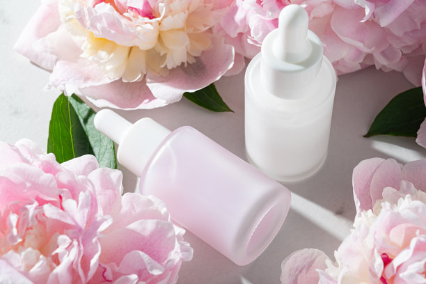 粉色牡丹花与精华瓶和面霜罐并排放置。柔和的植物护肤静物，适合春季系列和奢华品牌。图片下载