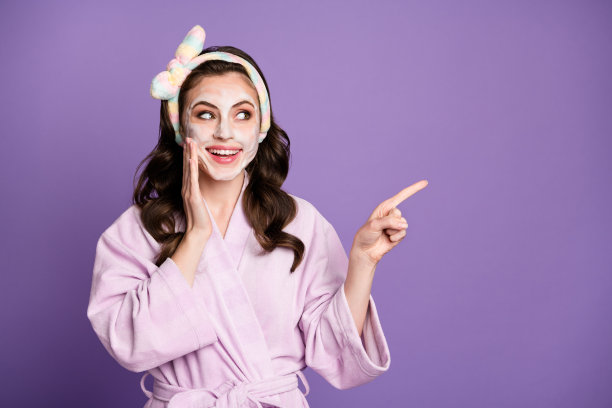 好奇微笑女孩涂抹面膜的照片肖像，展示空白区域，推荐在鲜艳的紫色背景上独立使用。图片下载