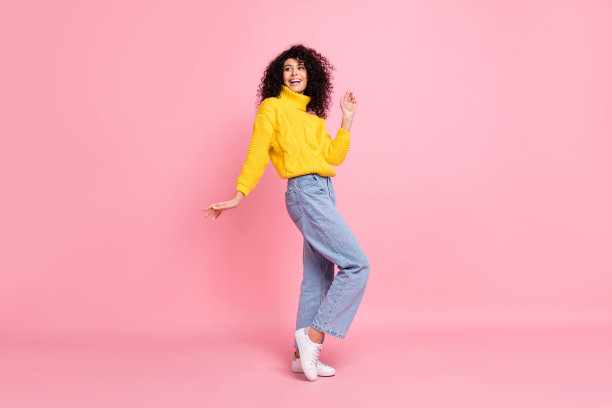 穿着黄色毛衣的有趣漂亮的波浪卷发女士在粉色背景下跳舞的全身照片图片下载