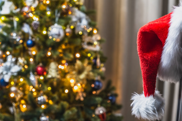 圣诞老人帽子挂在电视角落，背景是装饰着灯光的圣诞树。背景模糊，选择性对焦。图片下载