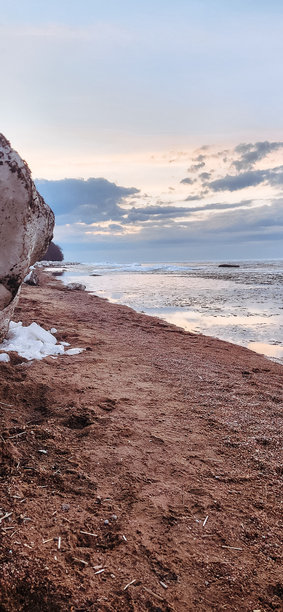春季风景。美丽的海湾黎明全景。明亮的光线下，水面上漂浮着积云。海岸线上有冰雪和岩石。阳光的光芒映照在海面上。竖版照片图片下载